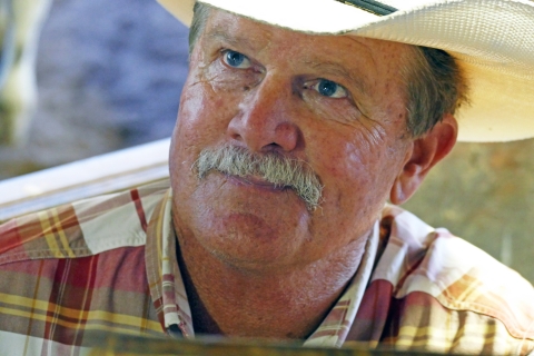 Male face smiling, wearing a hat and plaid shirt.