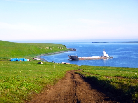 View of island and ocean, barge anchored at beach with storage containers ashore.