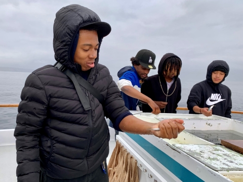 Young boys practice catching live sardines on the live bait tank on board a sea charter.