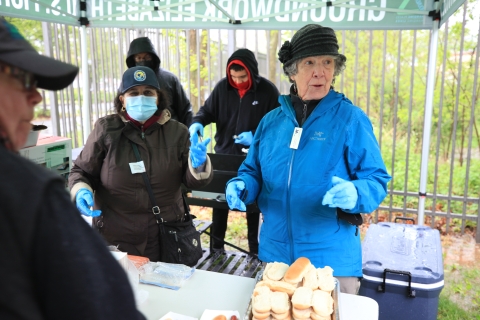 4 people stand under a tent serving food to event attendees