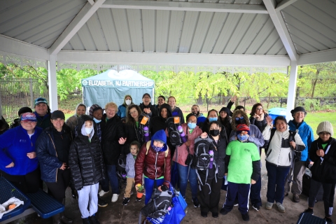 A large group of people standing under a pavilion smiling. A tent is seen in the background with the words "Elizabeth NJ Partnership" printed on the front