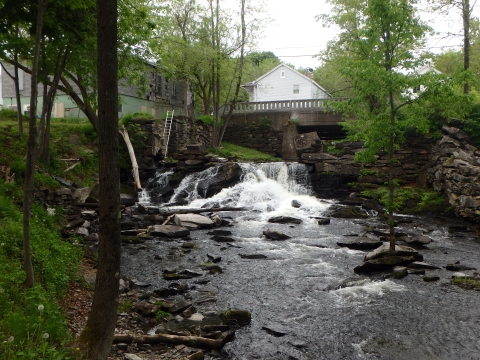 water flows over a rocky dam and under a bridge