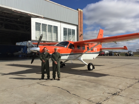 2 people stand in front of an airplane