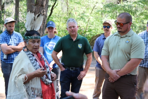 Several people stand in a circle around a woman wearing traditional Tribal garments