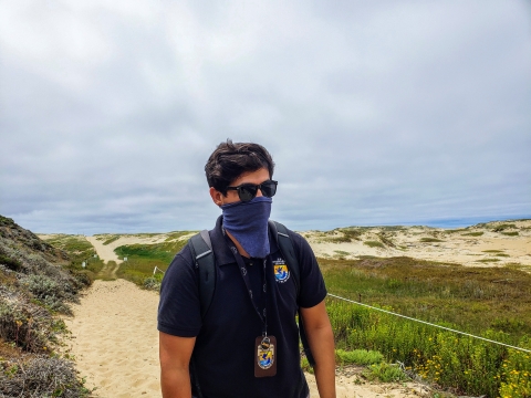 masked person with sunglasses and polo shirt with FWS shield walks through beach like path with native plants