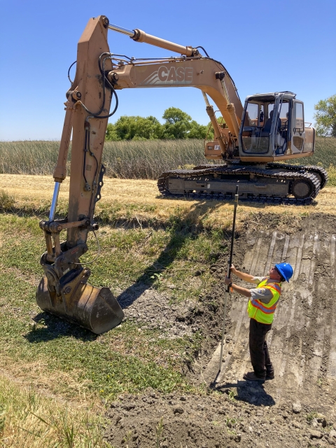 a man stands in a ditch next to a piece of heavy equipment