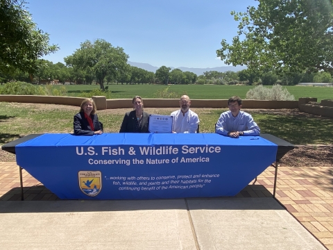 Two women and two men sit at a table holding up a signed document