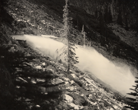 A black and white photo of a jet of water gushing over a rocky hillside.