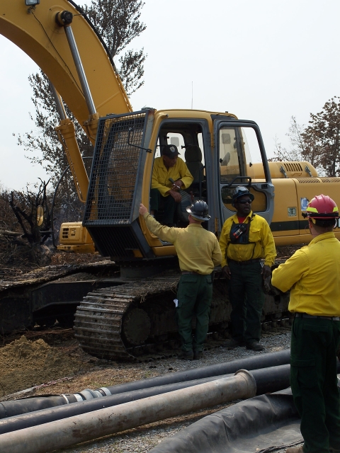 large yellow equipment with 4 men and large pipes laying on ground