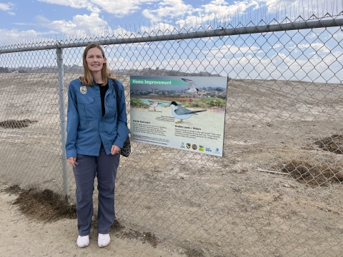 Woman stands in front of fenced area with large sandy hill inside