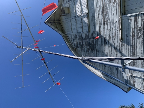 Photo looking up at an antenna array atop a slender pole, with a large old barn in the background.