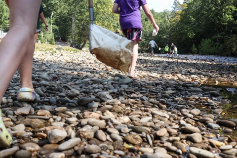 Students walking across a broad, rocky beach to a shallow river