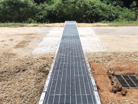 Metal grate running across a road with adjacent ground covered in straw.