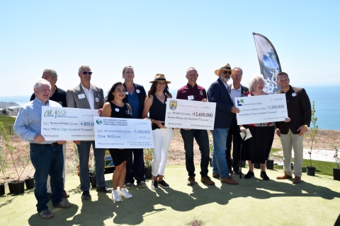 group photo of men and women holding oversized checks on side of hill