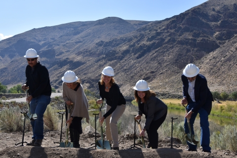 Fiver people hold shovels near water