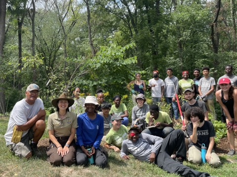 A large group of people kneel and stand in a forest, smiling at the camera.