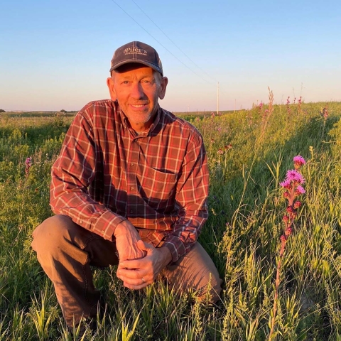 Craig Larson kneels on grasslands next to prairie flowers