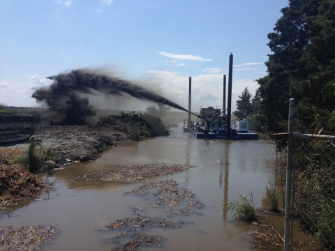 A barge spews sediment across a marsh, as it moves through a body of water