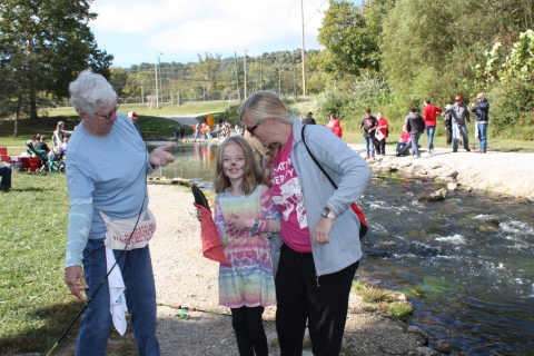 Student with teacher and volunteer holding a fish beside a stream