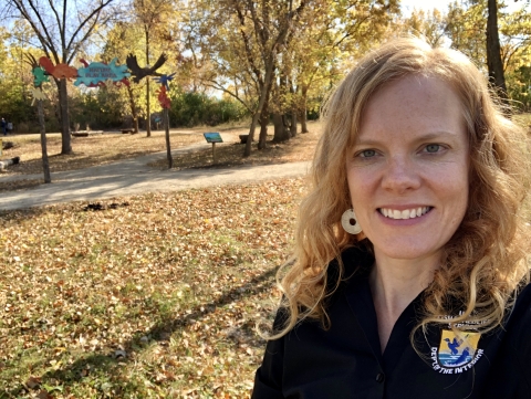 Person with blonde hair takes selfie with fall foliage in the background