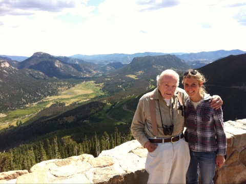 Two people pose at vista overlooking forest, mountains