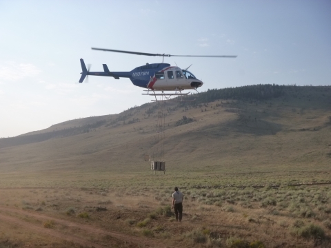 A helicopter takes off with a device hanging below full of fish to release