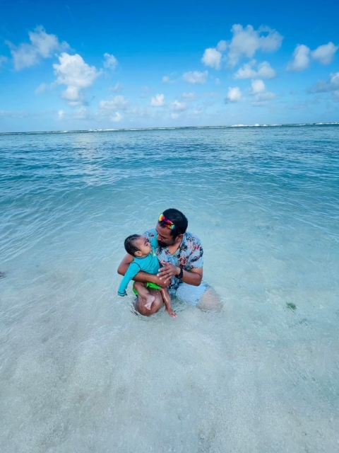 A father and their child sits in the ocean.