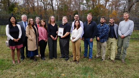 A group of people stand around a person holding a framed award certificate