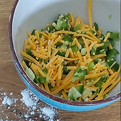 A bowl filled with a mixture of shredded cheddar cheese and diced jalapenos