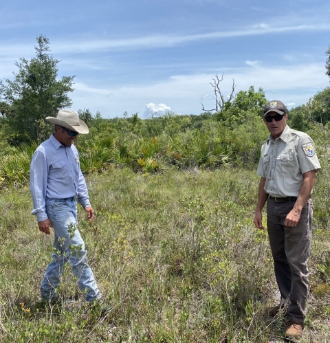 Two men, with hats, talking in a field. 