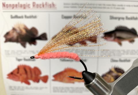 a fishing hook with gold and pink thread in front of a rockfish pamphlet