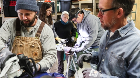 Two groups - one of two people, one of three people, each working on a chainsaw