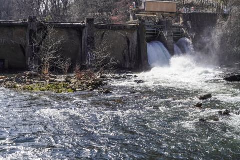 Downstream view of a dam stretching across a river, with water flowing through the right end