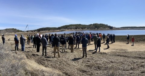 A crowd stands next to a marsh