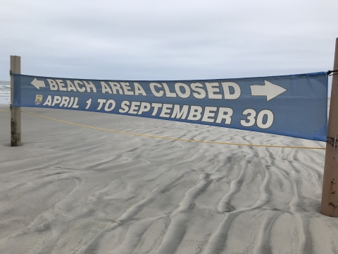 A blue banner on a beach informs the public of a beach closure from April 1 to September 30.