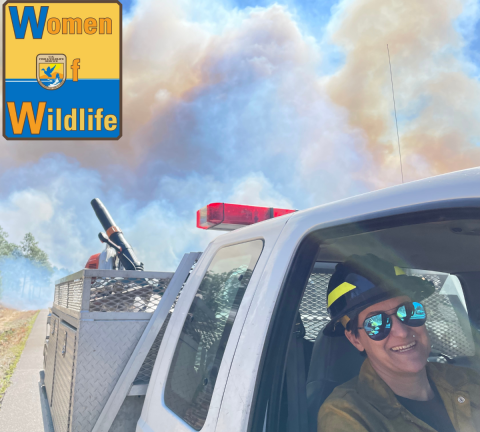 A person leaning out of the window of a white truck with smoke billowing in the background