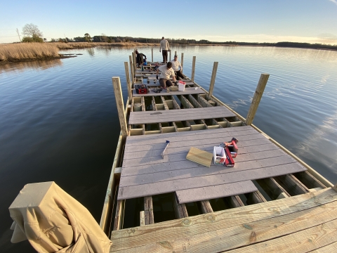 maintenance professionals stand and work on a semi-constructed wooden fishing pier that stretches out over open water