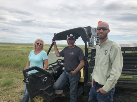 Jennifer and Chad Kunz with Curt Francis, all standing next to a utility vehicle on a grassland