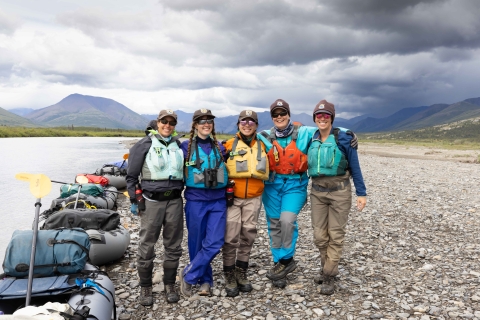 Five U.S. Fish and Wildlife Service employees pose for a group picture on the bank of a river with their rafts along the waterline. 