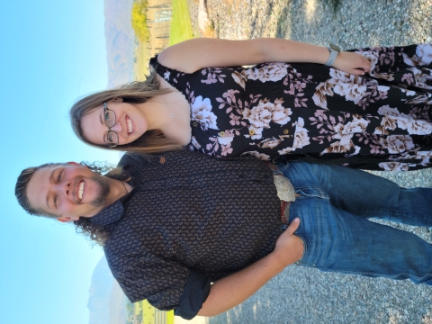 A man in a blue shirt and jeans is standing with a woman in a blue flowered dress. 