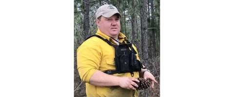 North Carolina Wildlife Resources Commission forester Casey Phillips holds a pinecone in a pine forest..