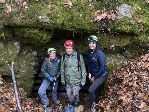 three people wearing helmets stand together near a large rock