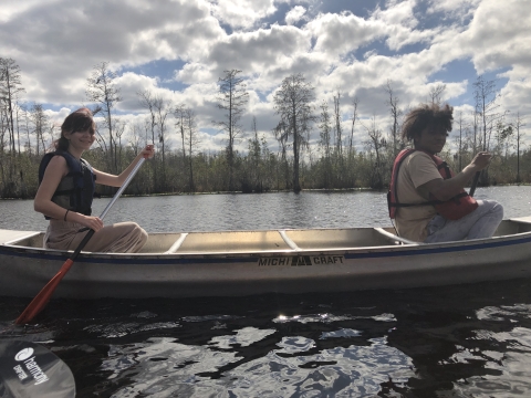 Two students smile as they work together to paddle a canoe on the Okefenokee swamp.