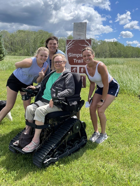 A large motorized wheelchair with multiple small wheels sits in front of a park sign.