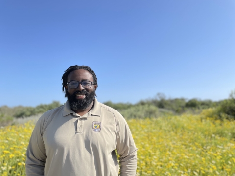 A man wearing a long sleeved polo stands in front of a field with golden flowers