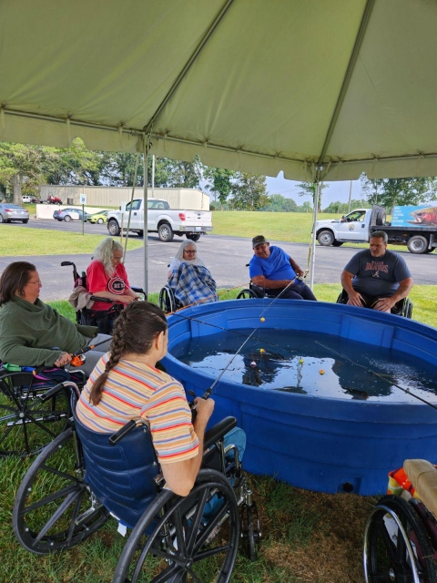 Elderly people fishing out of blue stock tub under a tent