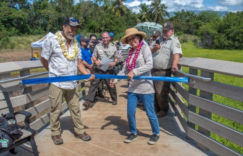 Pauline Kawamata from the Hawaiʻi Nature Center cuts the ceremonial ribbon at the rededication ceremony. USFWS staff and event attendees stand behind. 