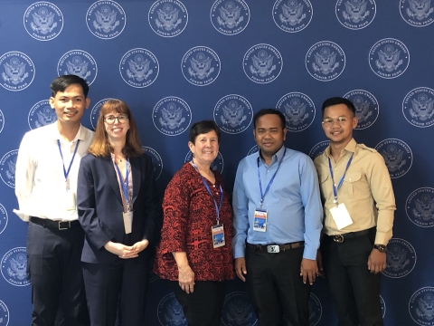 Five men and women wearing lanyards stand in a line and pose for a group photo