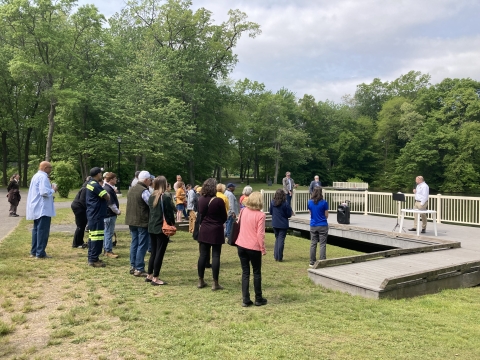 a group of community members stand in front of a platform by Keney Park Pond