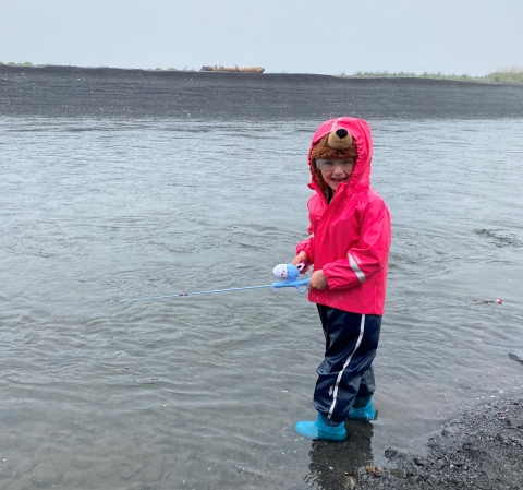 a girl holding a fishing rod stands on a river bank